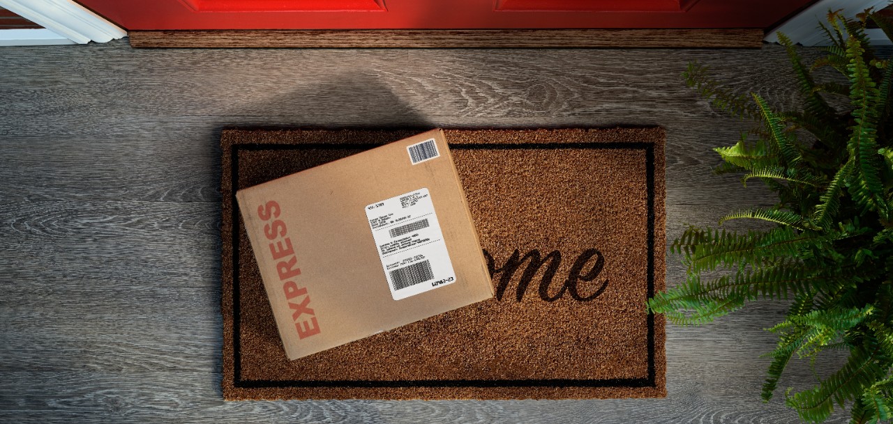 A stock image of a brown delivery box sitting on a welcome mat.