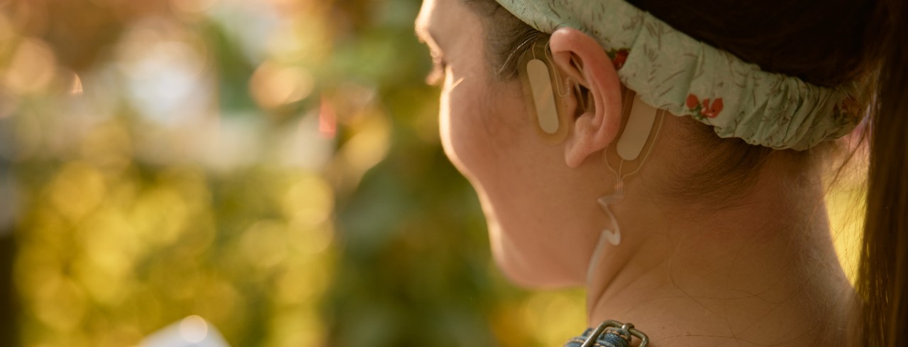 A woman wears the Sparrow Ascent device on her ear and holds the control device in her hand