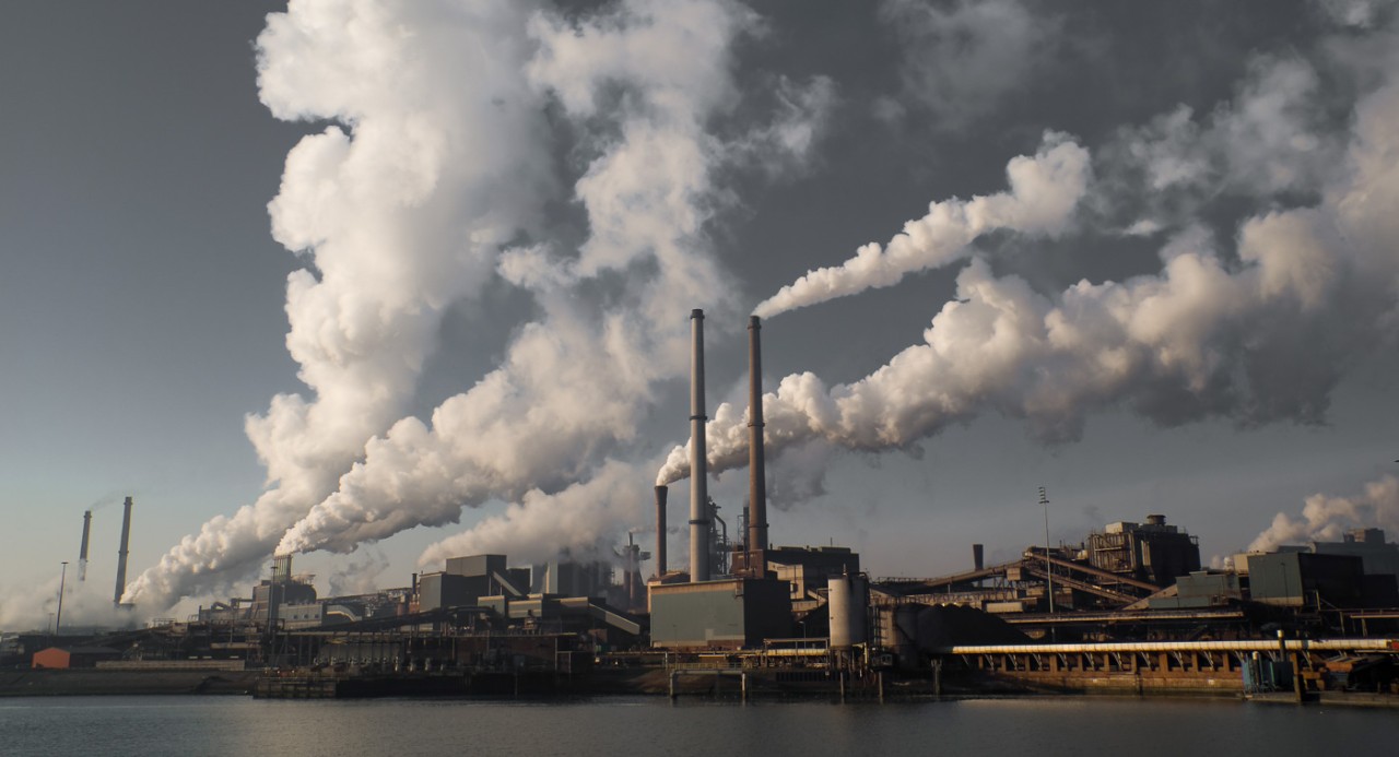 Clouds of emissions rise from smokestacks from a waterfront industrial complex. 