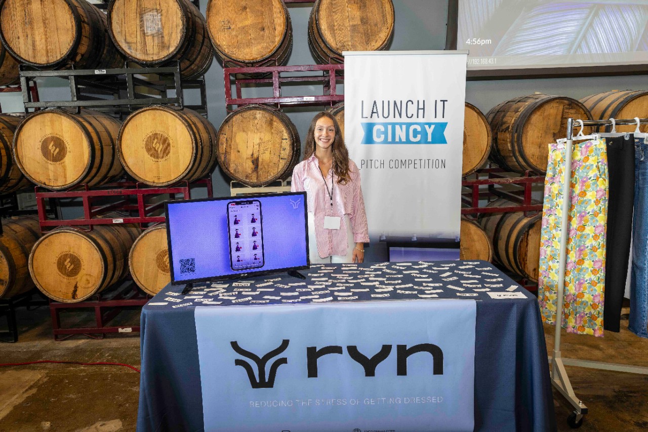 A woman stands behind a table displaying her startup business in a brewery.