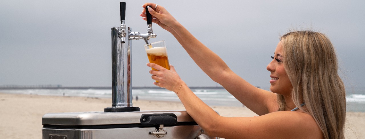 A woman on a beach pours a beer from the Cooler Keg