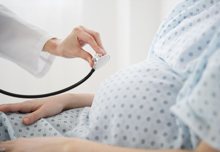 A photo of a pregnant woman in a hospital gown with a doctor using a stethoscope on her stomach