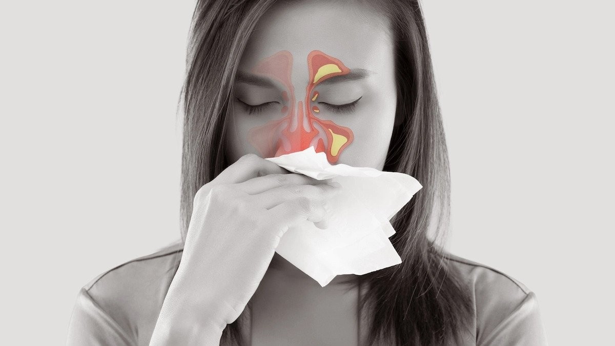 A photo showing a woman holding a tissue to her nose with sinus pain