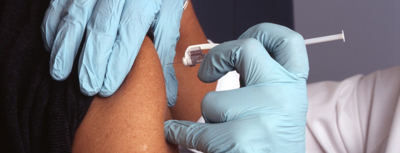 A health care worker wearing gloves gives a vaccine in a patient's upper arm