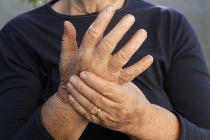 An elderly woman holds one hand in the other