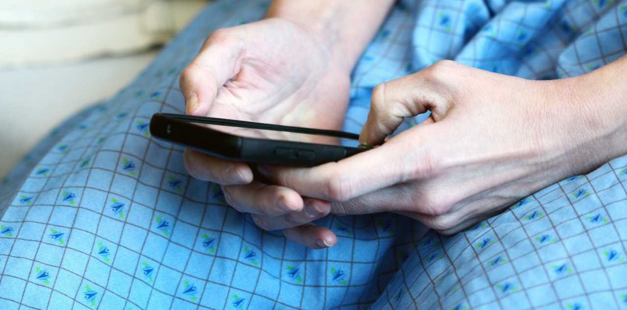 person sitting wearing a blue hospital gown using a cell phone 