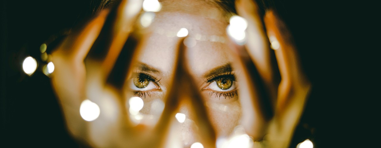 A woman's hands and eye look through a string of electric lights.