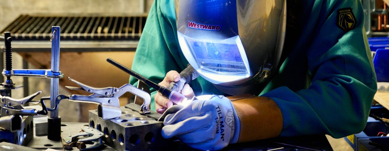 UC grad student Jacob Hoffmann wears shield and holds a welding iron in UC's Makerspace.