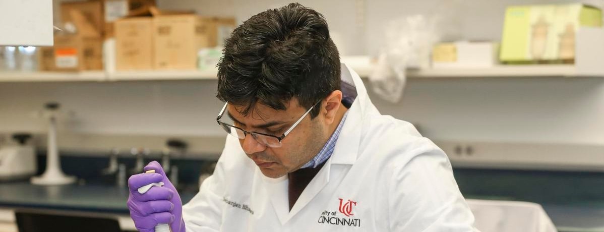 Debanjan Bhattacharya, wearing a lab coat and rubber gloves, pipettes a sample in the laboratory