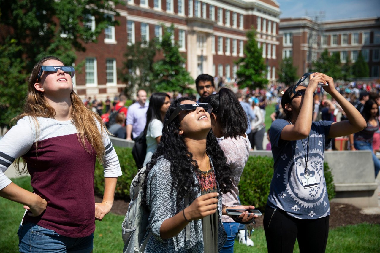 UC students wearing special glasses peer up a a partial eclipse from UC's Uptown Campus.