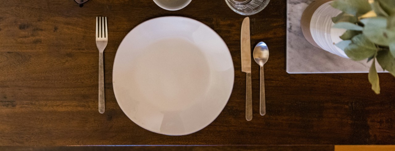 An empty plate with silverware and cups around it on a wooden table