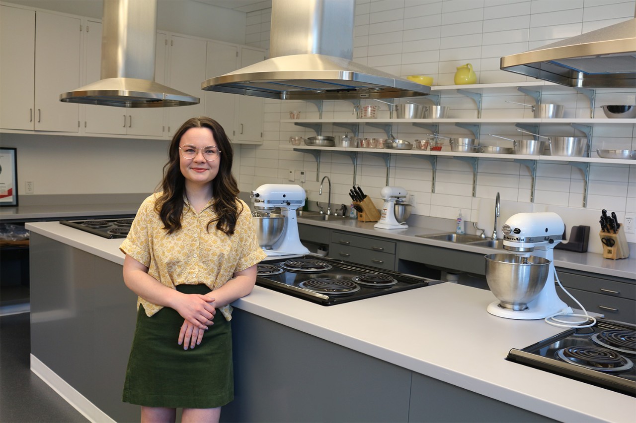 Adeline stands in the Foods Lab in front of a counter with stovetops and mixers