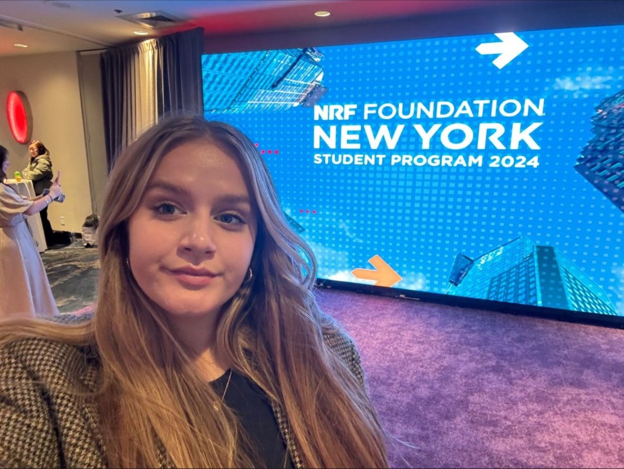 Kaylen Rolsen standing front of sign promoting a conference for  the National Retail Foundation in New York City