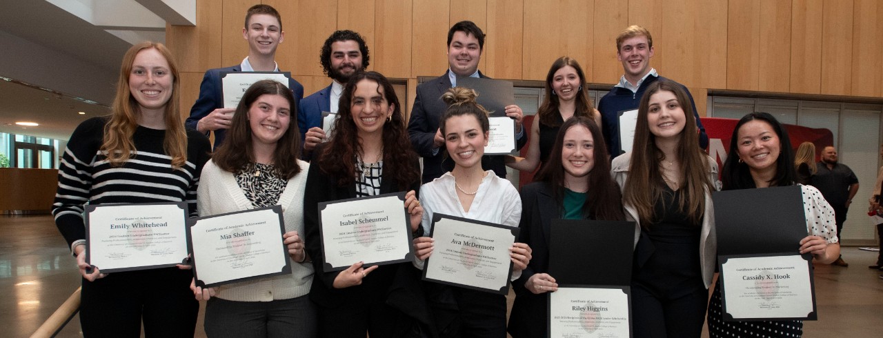 Twelve students with seven standing in the front row and five in the back row hold up their recognition certificates