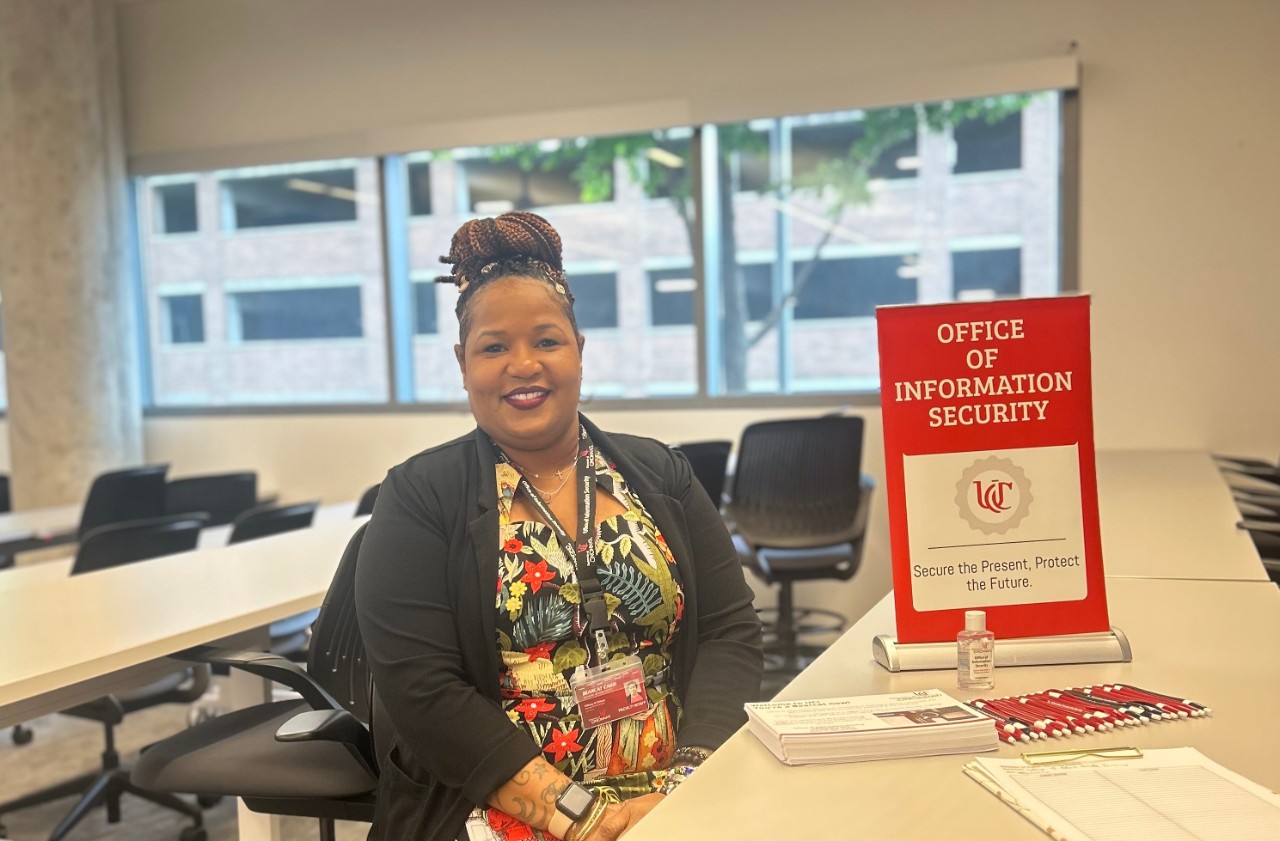 Information Security Roadshow presenter Tiffiany Wilson next to an Office of Information Security banner that reads "Secure Present, Protect the Future."