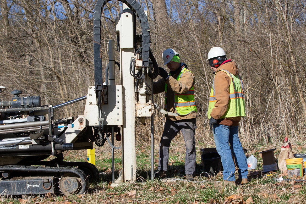 Workers use equipment to dig a monitoring well. 