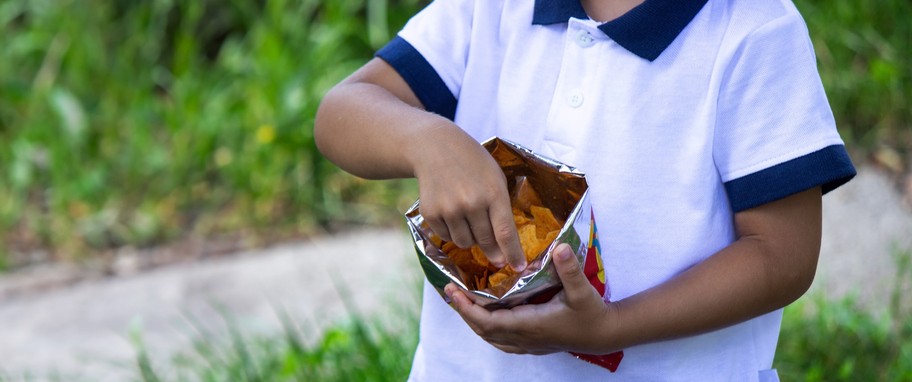 A child reaches into a bag of chips with their hand