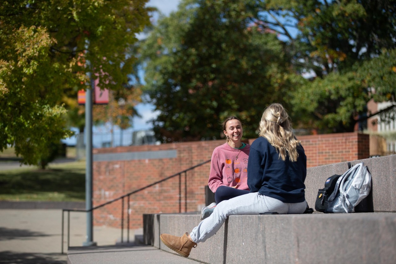 Two students shown sitting on the UC campus chatting