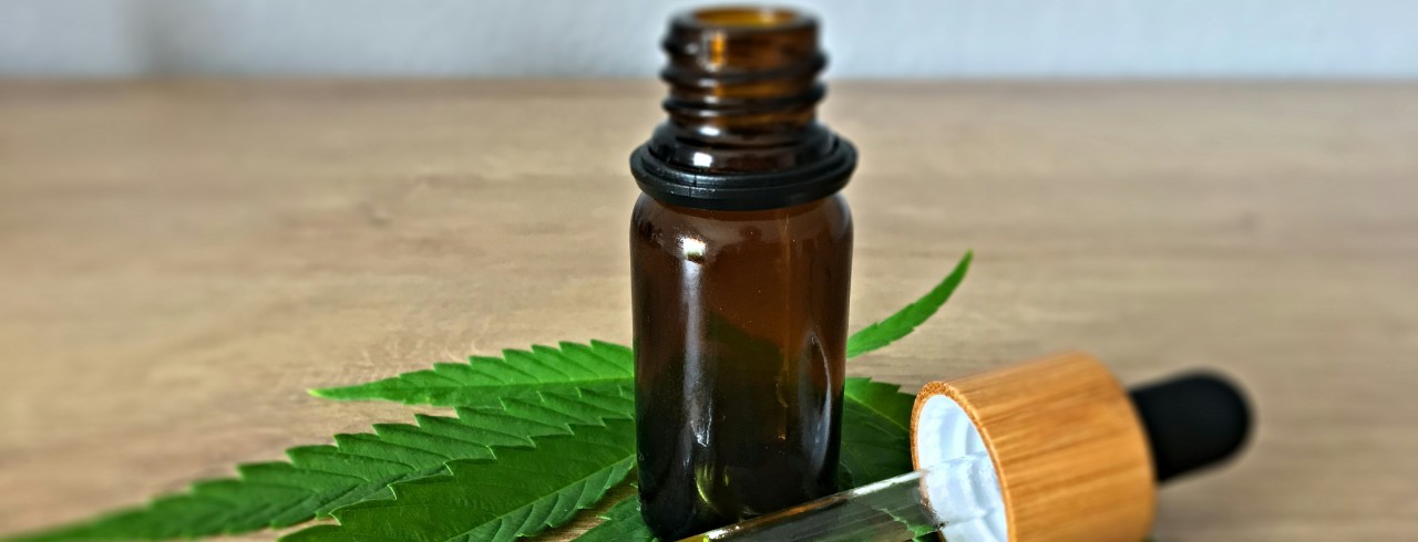 A brown tinted glass bottle and dropper of CBD oil on top of a marijuana leaf
