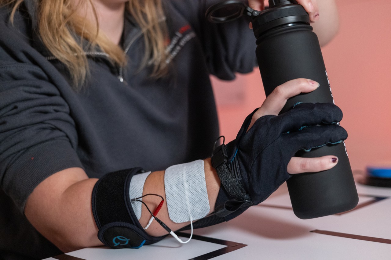 A student, wearing an exoskeleton prototype, picks up a black water bottle