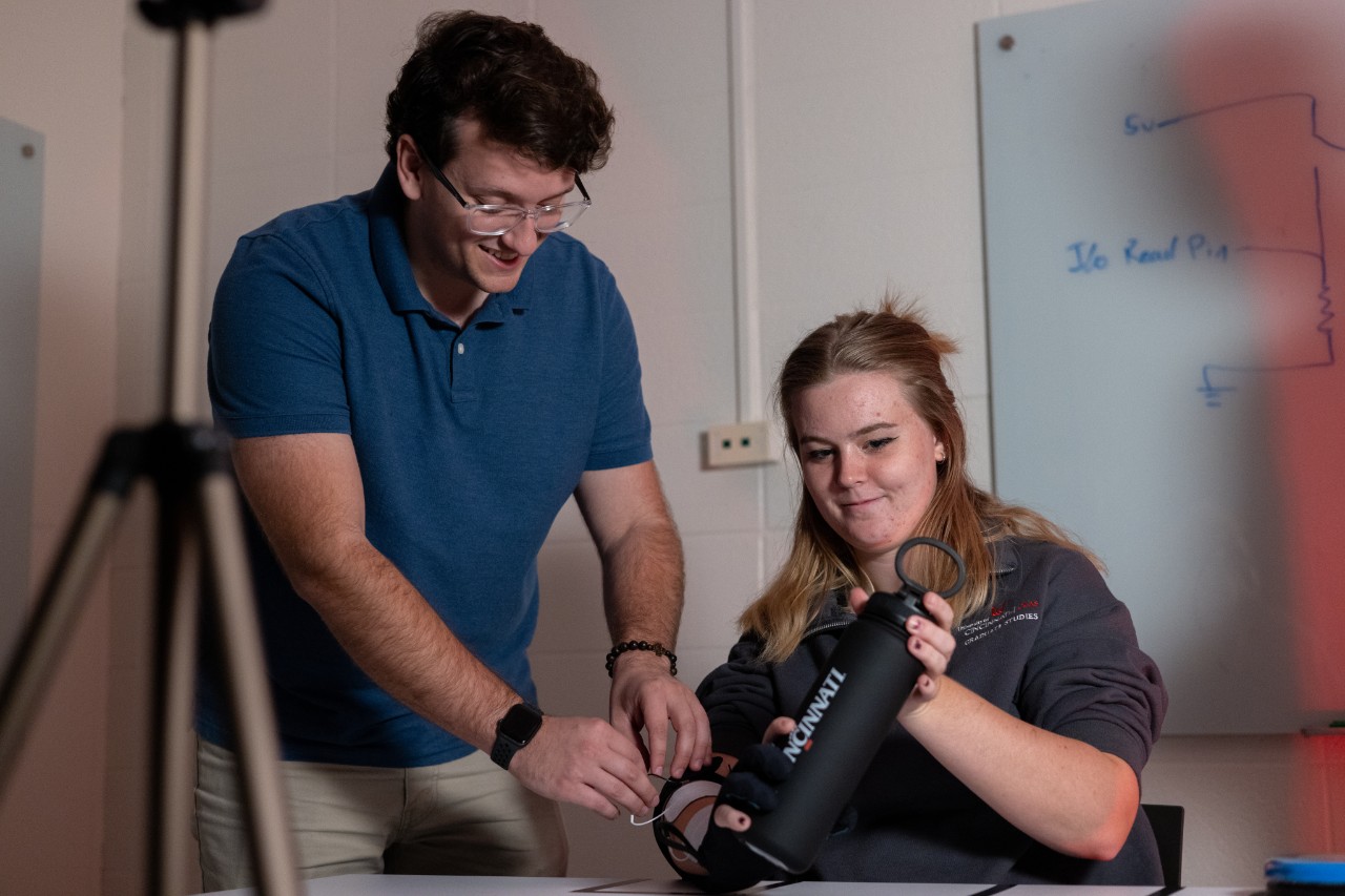 Ryan Cuda stands and adjusts the exoskeleton a student is wearing