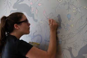 Woman painting colorful figures on a gray wall.