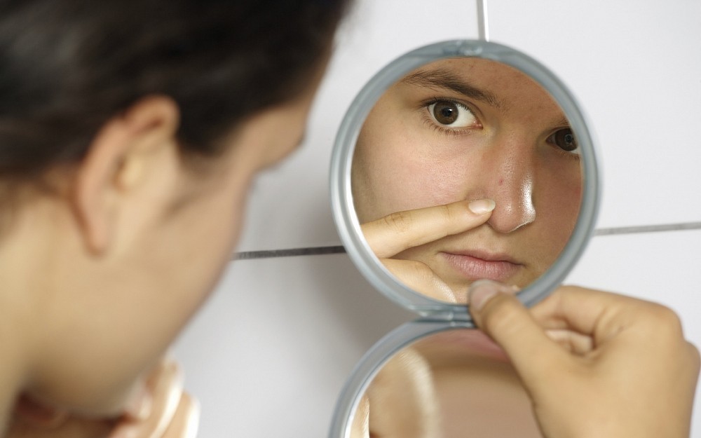 Young female looking at blemish in mirror