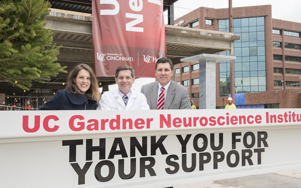 Joe Broderick, MD, center, director of the UC Gardner Neuroscience Institute, stand by the final beam along with Adana Johns and Clark Miller of Perkins+Will, the architect for the new outpatient facility